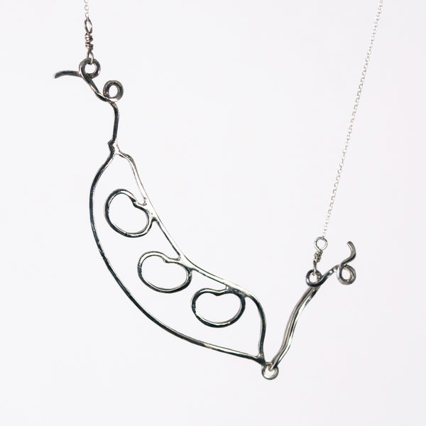 The silver Bean Pod Necklace has an outline of a peapod with three beans on the inside. Symbolic sentimental jewelry that helps you celebrate all the people in your pod. From a collection of fun and playful kinetic silver bean jewelry by Tinker Company.