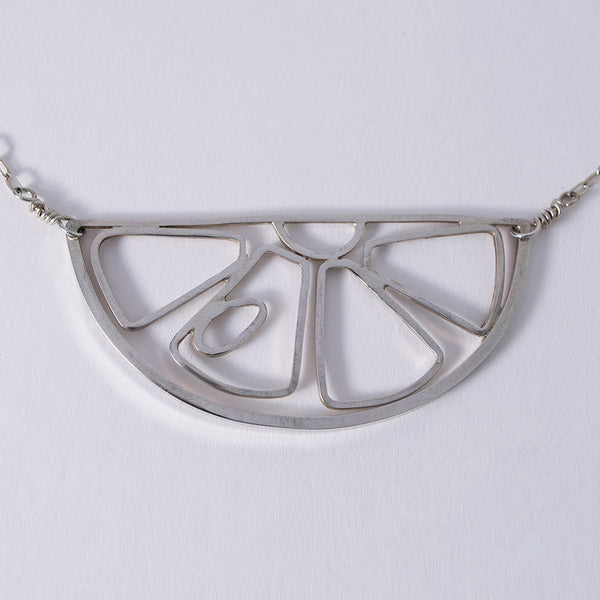 A silver pendant in the outline of a citrus fruit slice