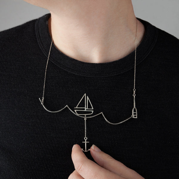 Model wears the Sailing Necklace with a Moving Sailboat and uses the anchor to move the boat across the wave. From a collection of fun and playful kinetic jewelry by Tinker Company.