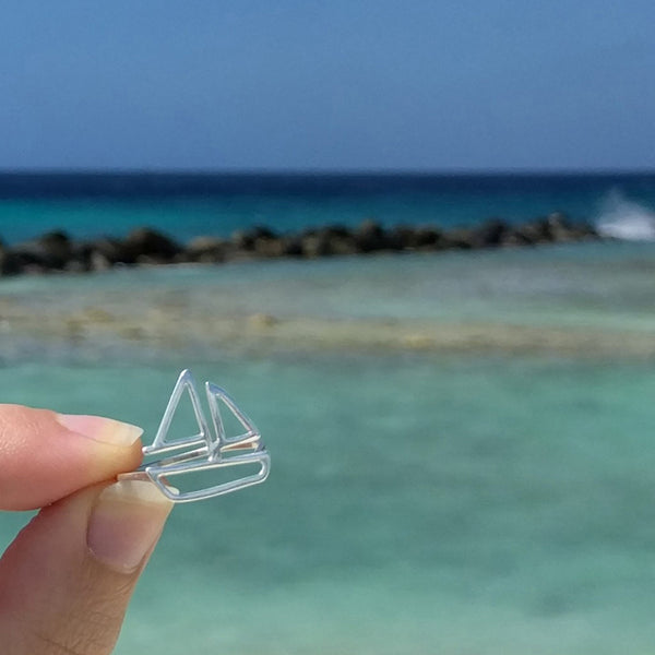 Model holds a silver Sailboat Ring by Tinker Company in front of the Caribbean blue water at the beach. Wearing fun and playful nautical jewelry is the perfect way to remember your last summer beach vacation and daydream about the next one.