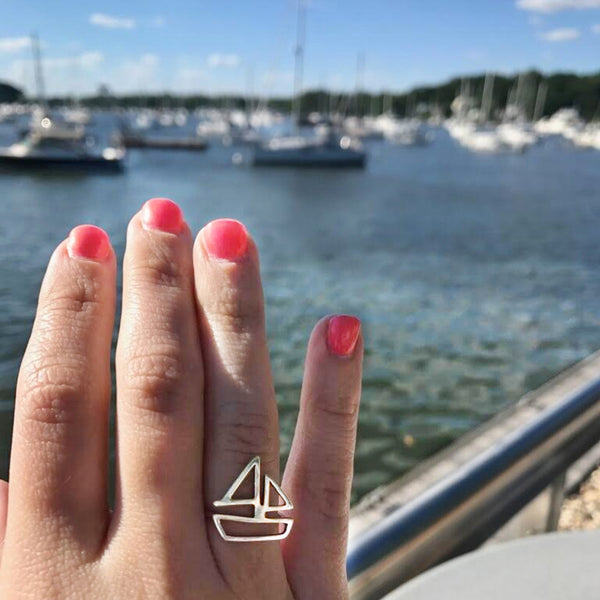Sailboat Ring in sterling silver by Tinker Company, shown on model's hand at the marina with sailboats and water in the background.
