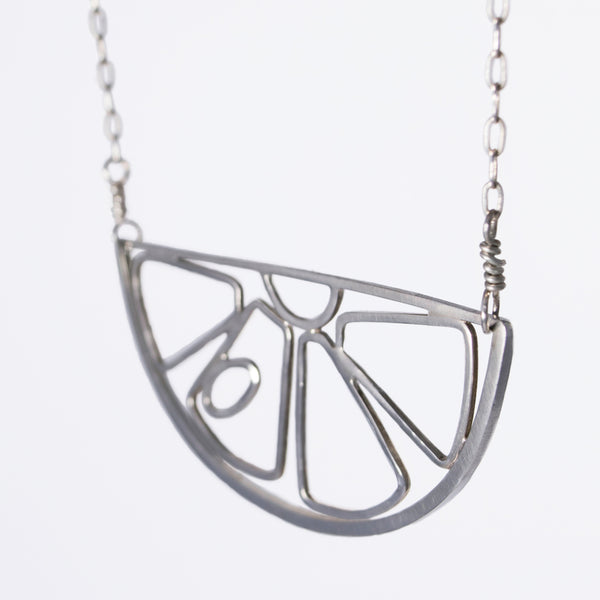 Silver pendant necklace in the outline of a citrus fruit slice, part of a collection of playful and whimsical memory jewelry by Tinker Company.