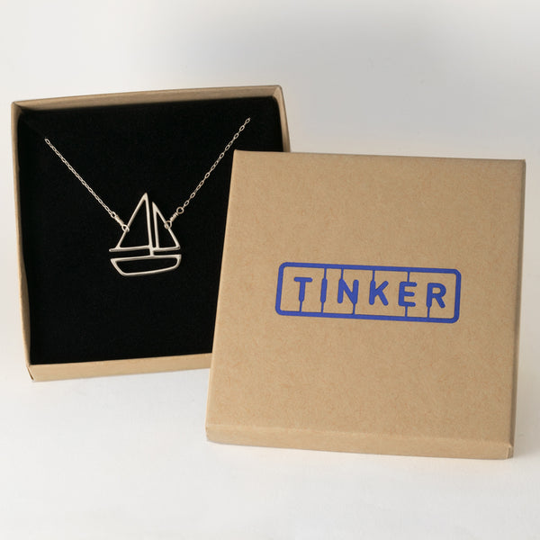 Sterling Silver Sailboat Pendant necklace has an outline of a boat on delicate chain. From a collection of playful sailing memory jewelry shown in a Tinker Company gift box.