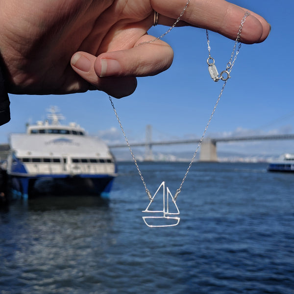 Silver Sailboat charm pendant necklace with the San Francisco ferry boat and Bay Bridge at the SF Ferry Building Pier. Sentimental storytelling memory jewelry to remind you of your favorite memories on the water. Perfect for your coastal style capsule wardrobe. From a collection of fun and playful nautical jewelry by Tinker Company.