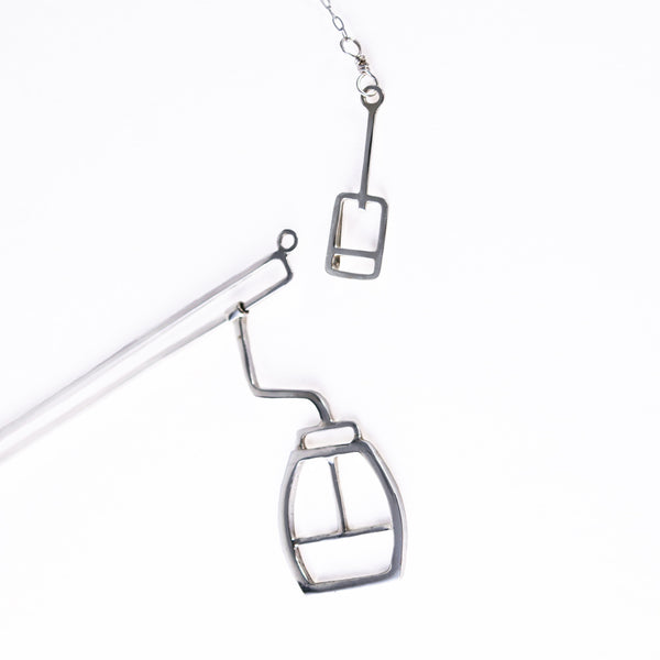 Details of Tinker Company's silver skiing necklace show the moving gondola and ski lift ticket clasp. Fun and playful apres-ski jewelry for snowboarders and skiers with winter vacation wanderlust. Designs that remind you of your favorite memories spent on the mountain.