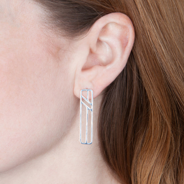 Model wears the Telephone Pole Earrings in sterling silver by Tinker Company. Part of a collection of abstract geometric jewelry celebrating the everyday things that connect us. Minimalist, not meaningless.