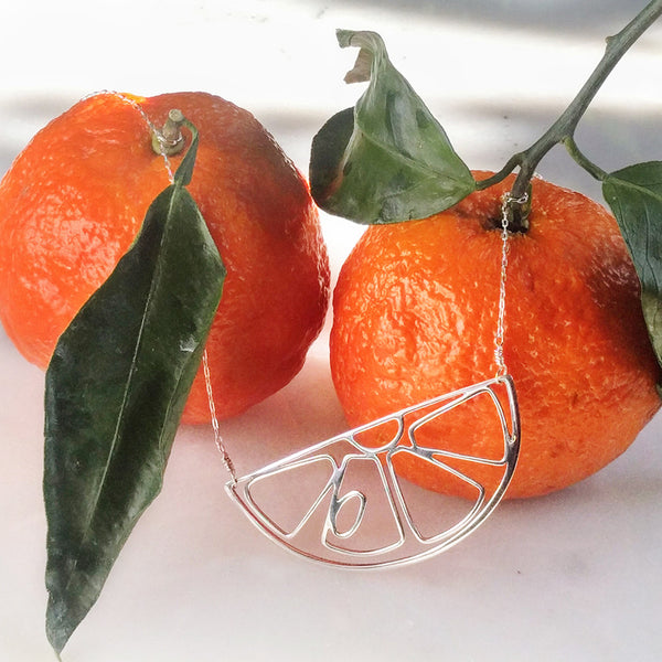Tinker Company's Citrus Slice Necklace shown with two satsumas