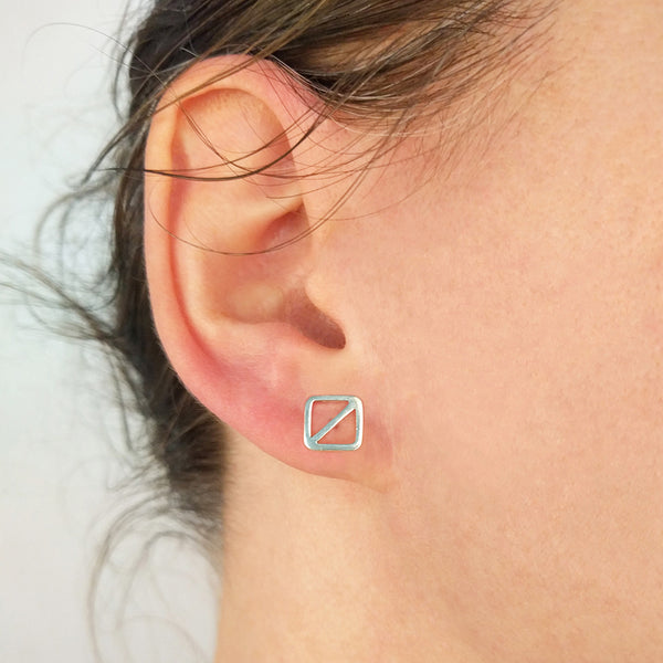 Geometric nautical earrings in a square shape with a diagonal line, the minimal design inspired by the letter "O" nautical flag which is the maritime signal flag for "man overboard!" Part of the Marina Collection designed by Tinker Company. Shown here in sterling silver on a model's ear.