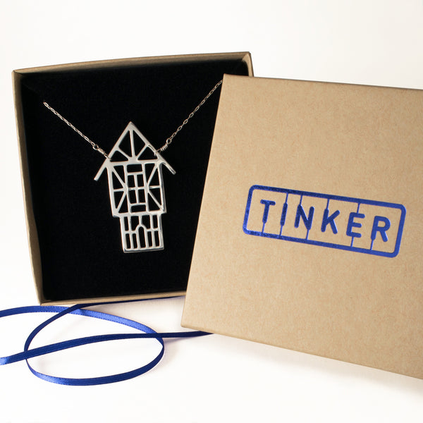 Tudor Ski Chalet Necklace shown in a Tinker box with blue ribbon. The perfect gift for your favorite skier or snowboarder.