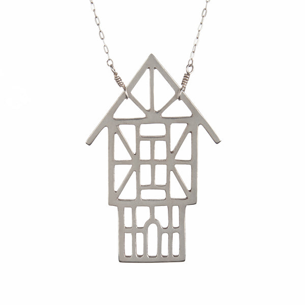 The Tudor Ski Chalet Necklace is a sterling silver outline of a Tudor style house designed and made by Tinker to capture your favorite winter vacation memories.
